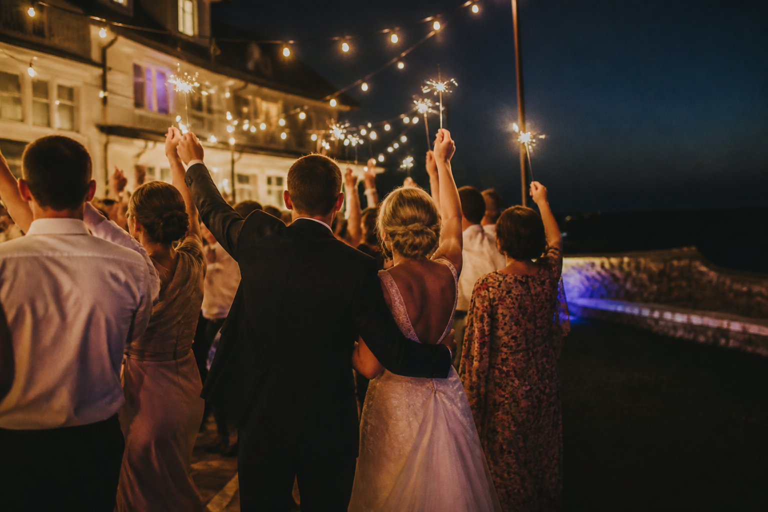 A warmly lit wedding celebration viewed from behind the guests